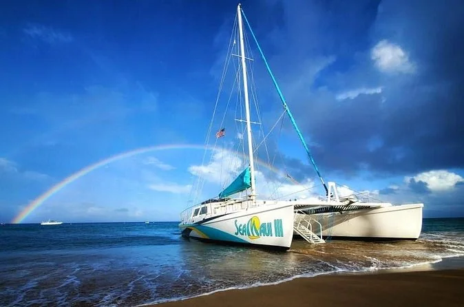A Sea Maui catamaran pulled up on the sand under a rainbow