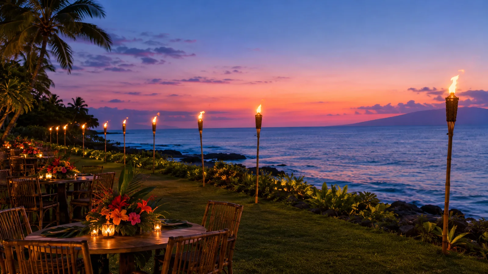 Tiki torches and flower-dressed tables on an oceanfront lawn at blue hour