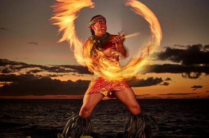 A fire-knife dancer spinning flames against a sunset over the sea
