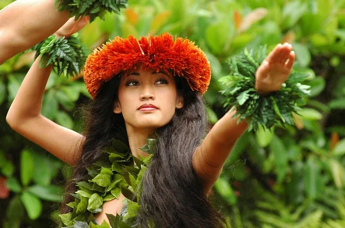 A hula dancer in a red flower crown with leaf bracelets