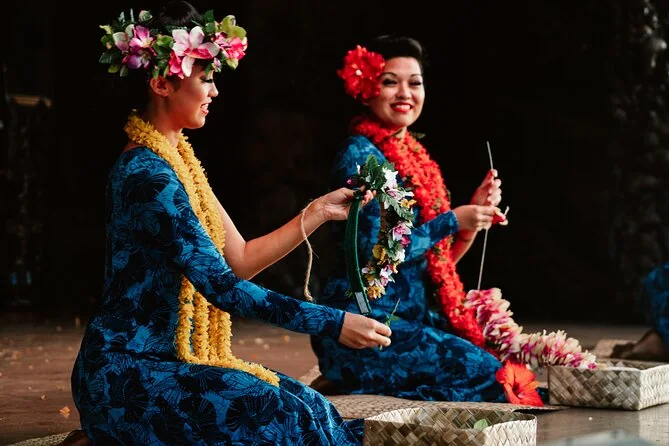 Two performers in blue dresses and lei making flower lei on stage