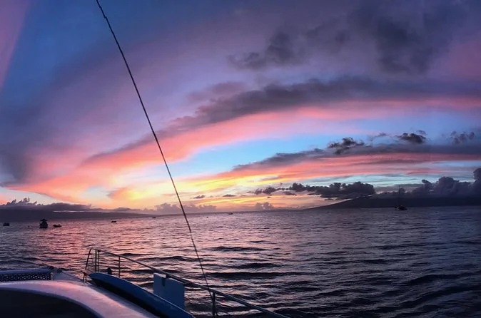 A pink and violet sunset over the sea seen from a catamaran deck